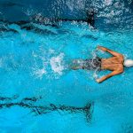 Top view of a swimmer wearing a cap, performing a front crawl stroke in a clear blue swimming pool.